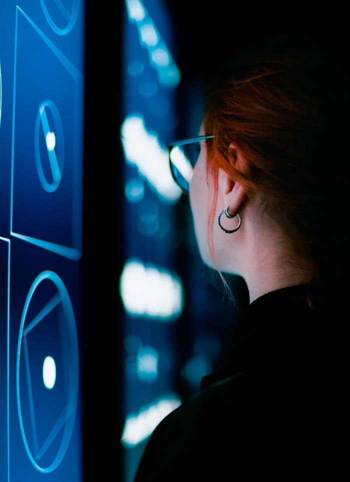 services-img A woman with eyeglasses interacts with an illuminated digital screen, showcasing modern technology.