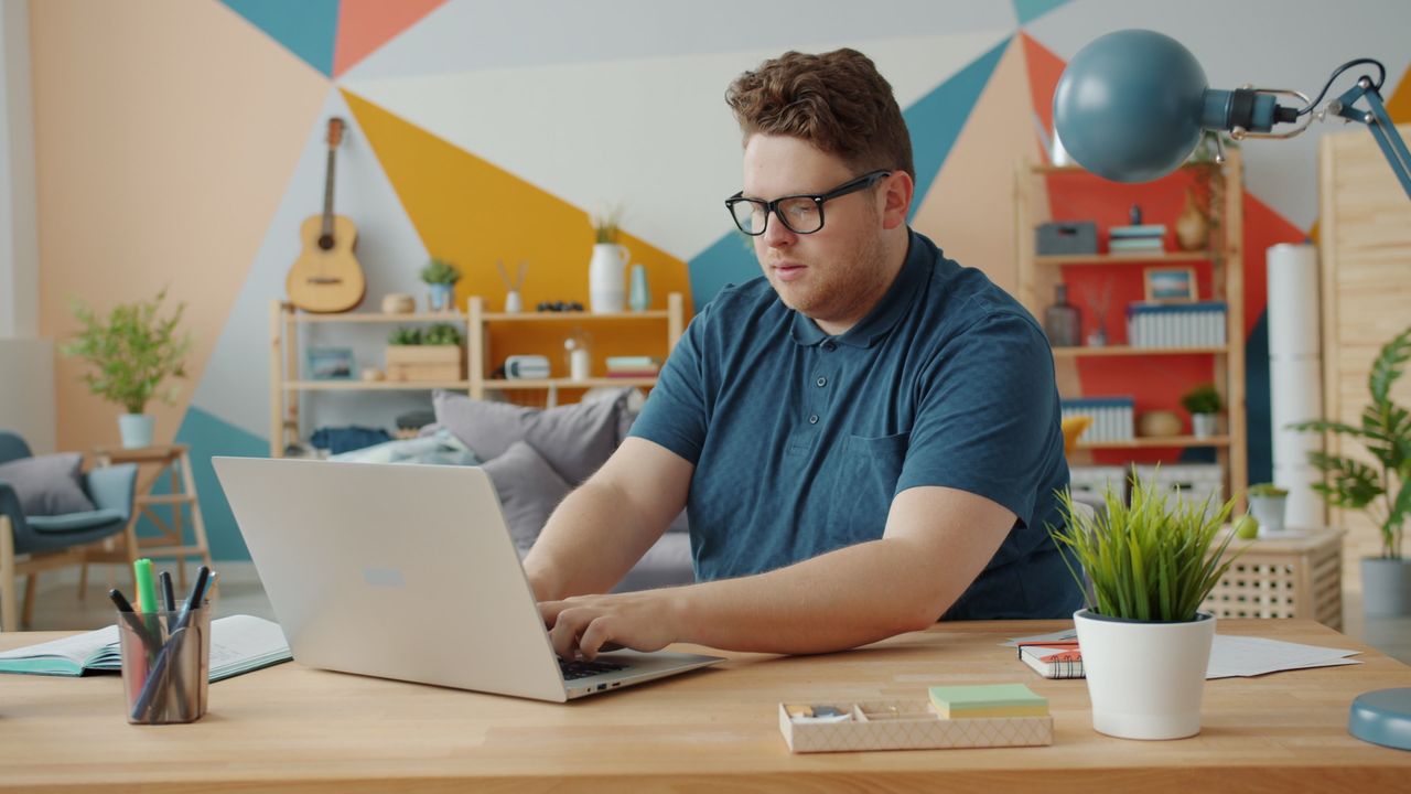 A young man focused on working at his laptop in a stylish, colorful office setup.